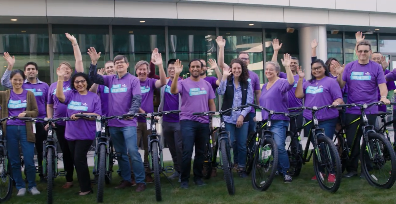A group of Vertex Volunteers waving and standing next to bicycles they built media item